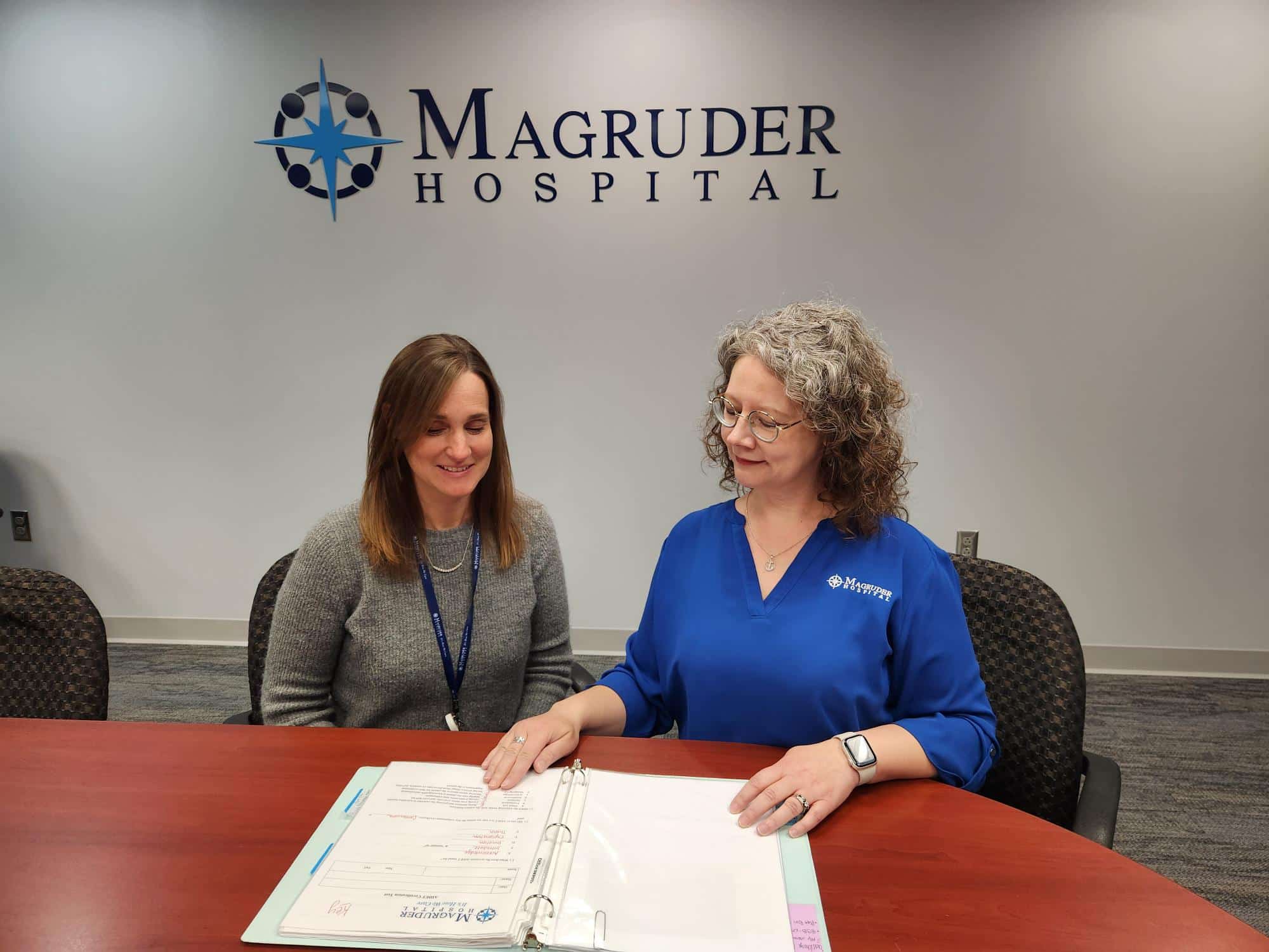 Two healthcare administrative workers talking at a table about employee HR benefits