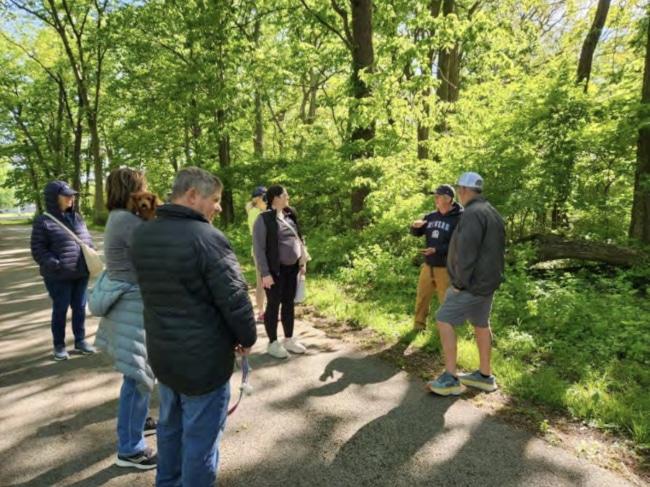 several people walking and talking on a trail through the forest